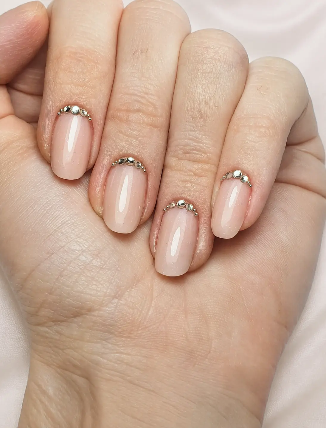 Ovale Nägel in Nude, am Nagelbett ein Bogen aus goldenen Kristallen.